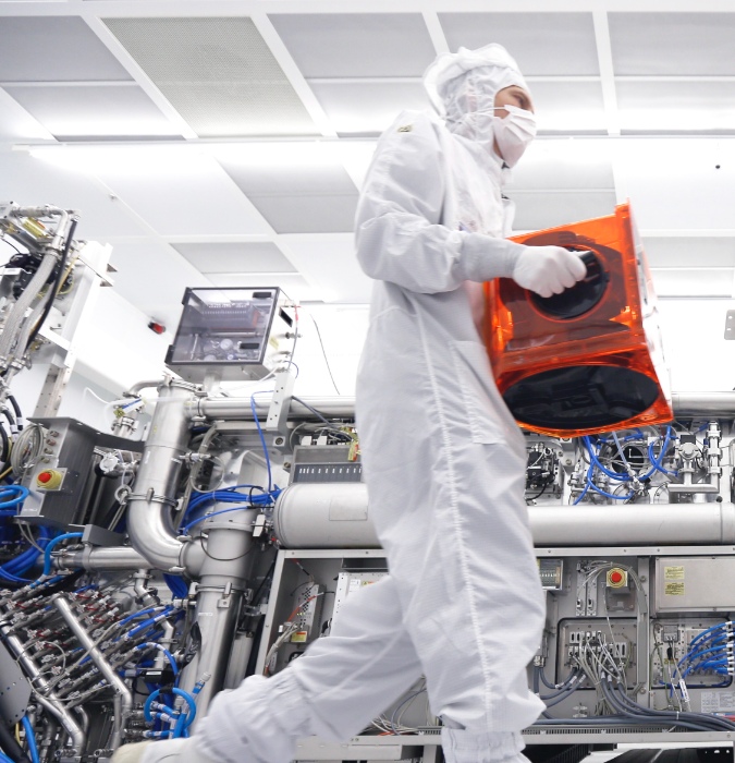 ASML man in bedrijfskleding verplaatste een doos in 'the clean box room'.  The enable affordable microelectronics that improve the quality of life. They invent, develop, manufacture in service advanced technology for high-tech lithography, metrology and software solutions for the semiconductor industry. 